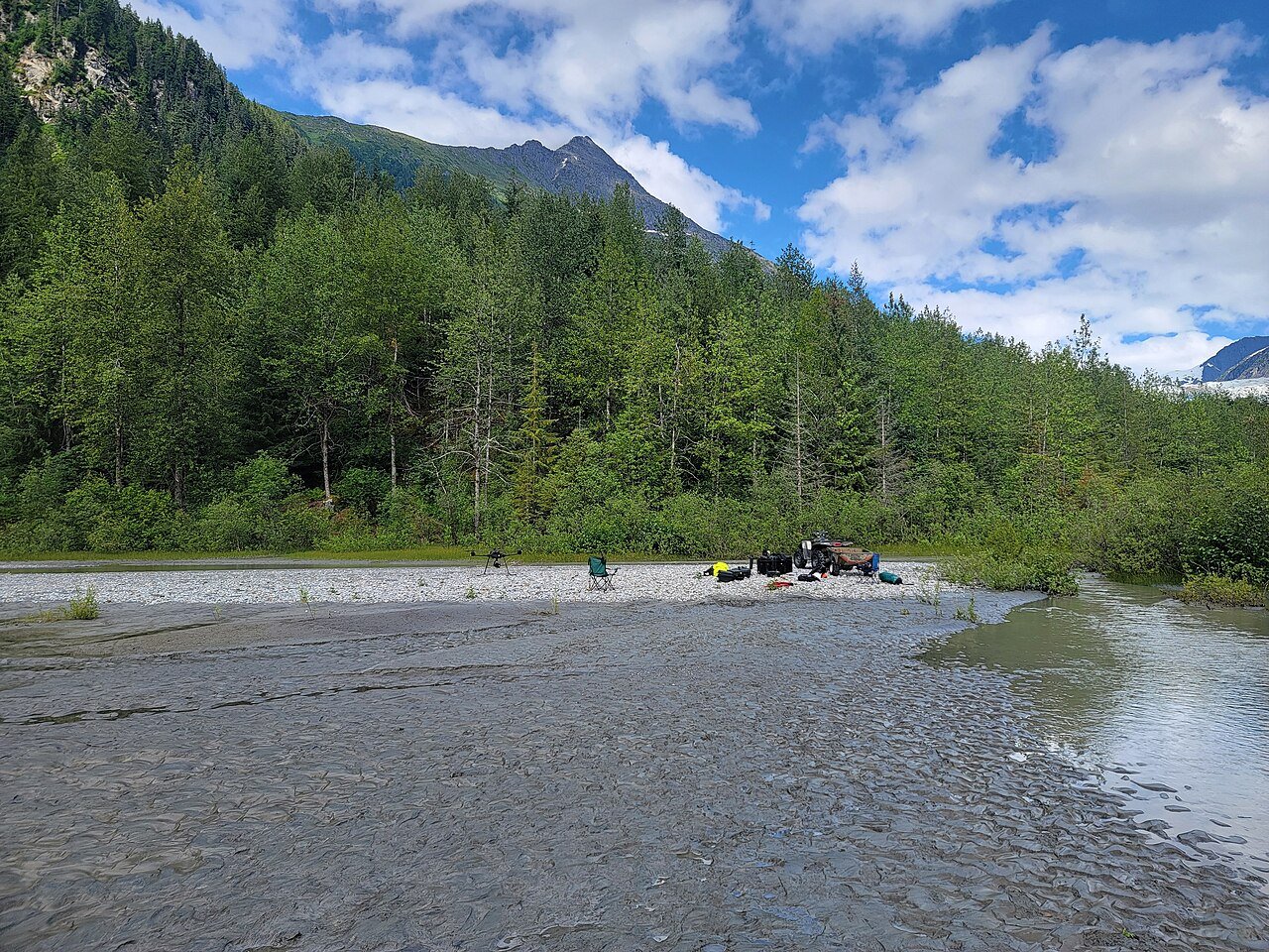 A mapping drone deployed on a gravel bar in a mountain valley for a survey mission, with field gear laid out beside it
