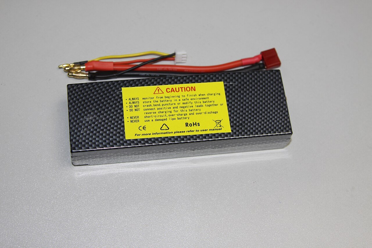 A hard-case lithium polymer battery pack with balance lead and power connector, showing the printed safety caution label